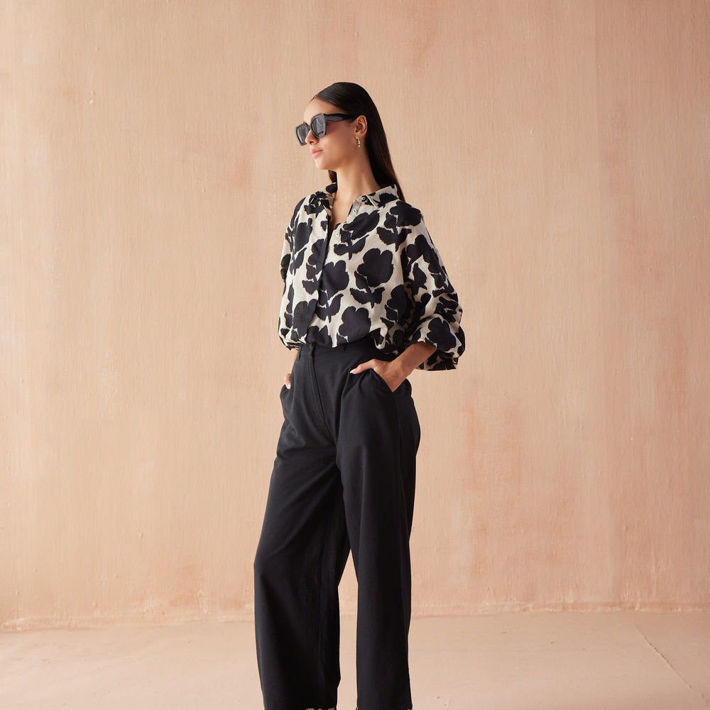 Front three-quarter view of model wearing the Nero Blouse in Emma, a button-front black blouse tucked into wide-leg black trousers.