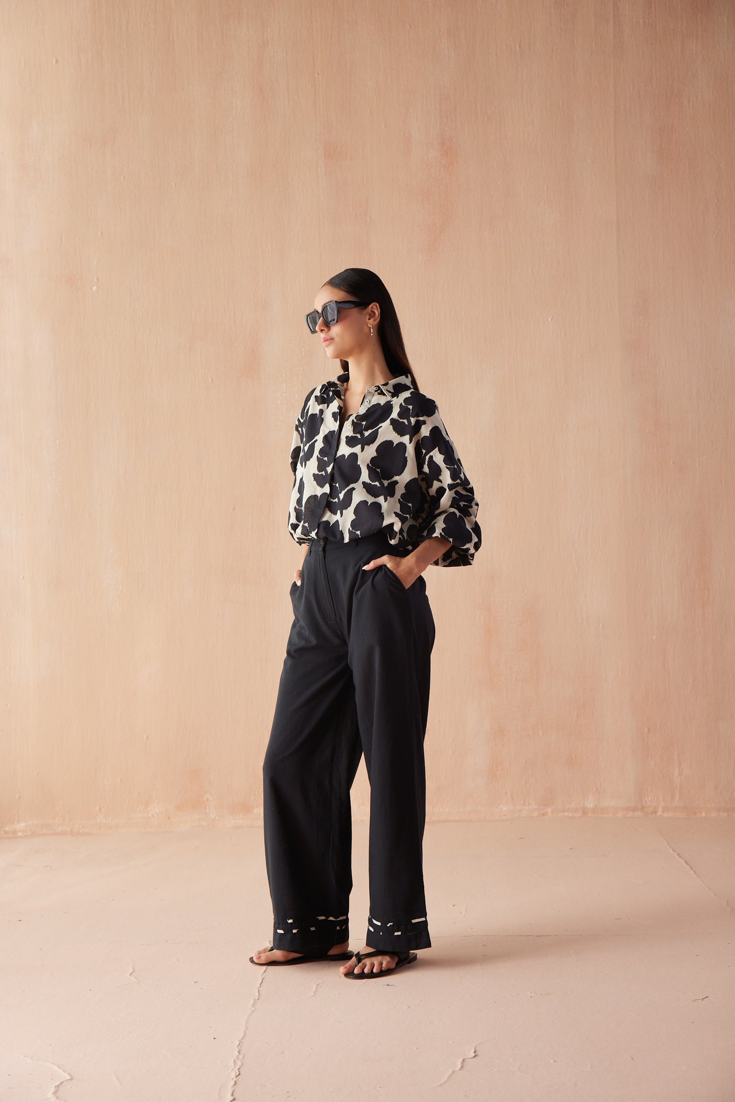Front three-quarter view of model wearing the Nero Blouse in Emma, a button-front black blouse tucked into wide-leg black trousers.