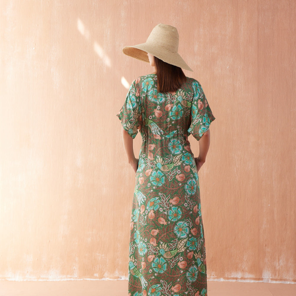 Back view of Pia Caftan in Kala Kelp, ankle-length green floral caftan with short sleeves and drawstring waist, styled with straw hat.