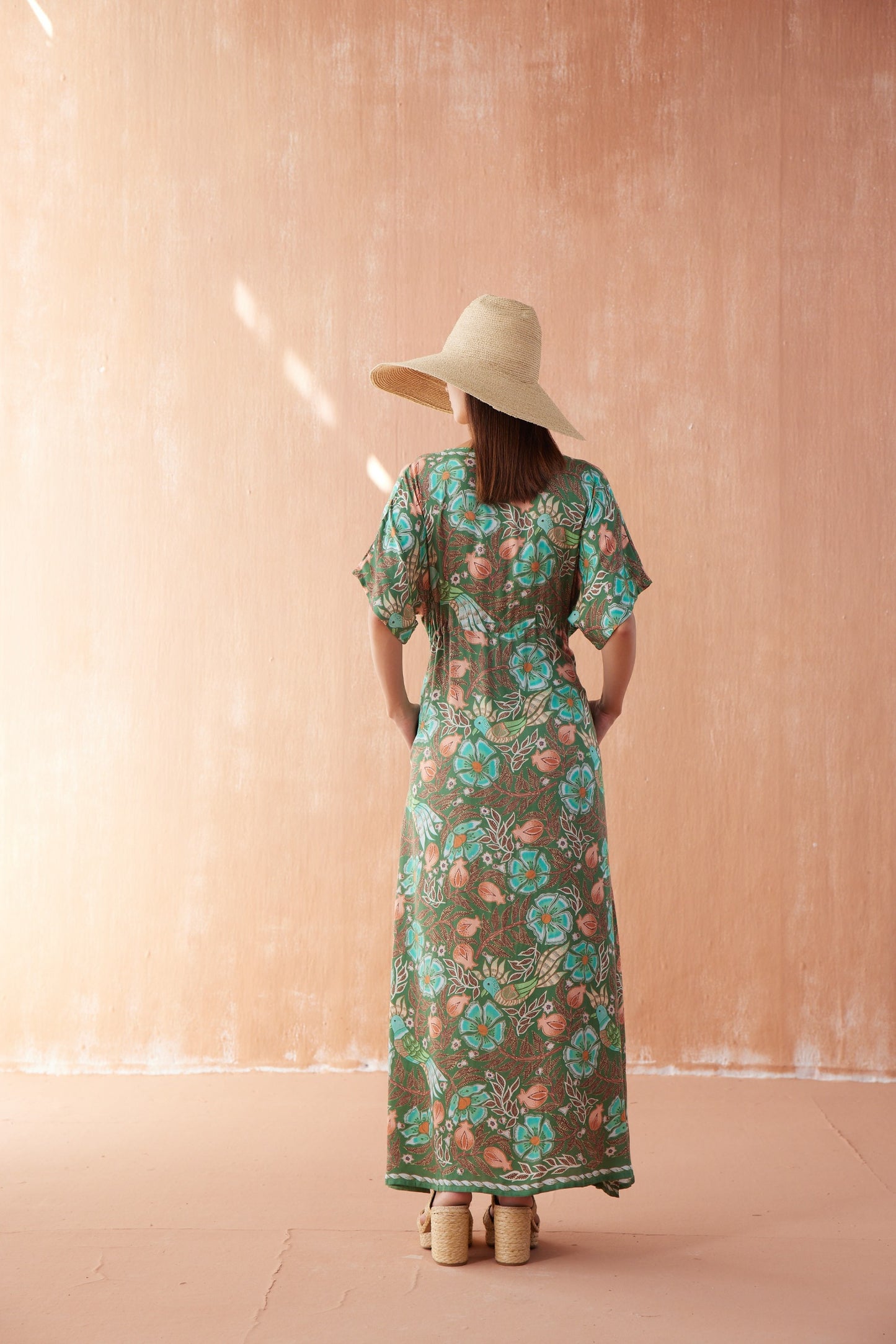 Back view of Pia Caftan in Kala Kelp, ankle-length green floral caftan with short sleeves and drawstring waist, styled with straw hat.