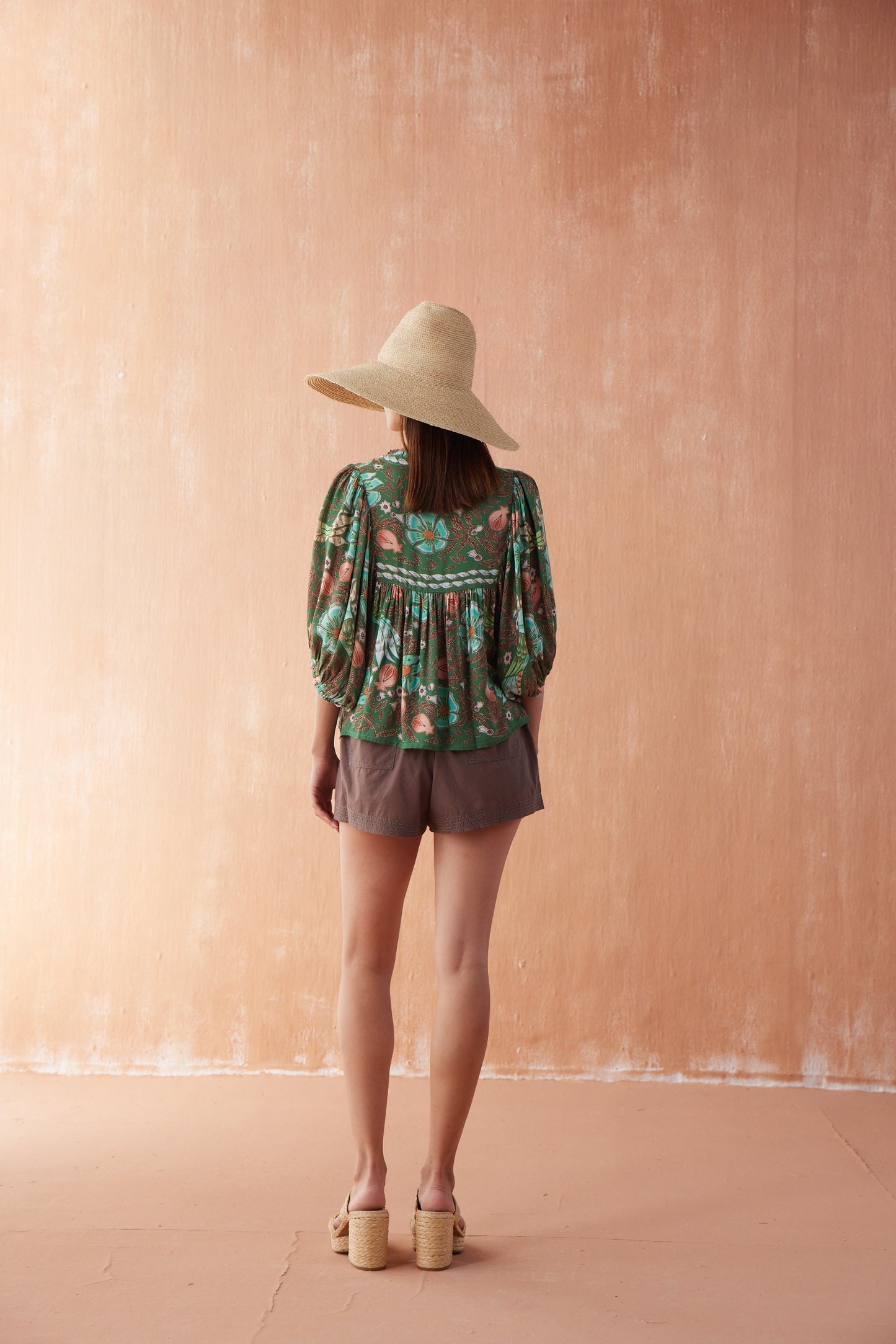 Back view of Nero Blouse in Emma, a collared black blouse with abstract floral print, styled with matching shorts and sun hat.