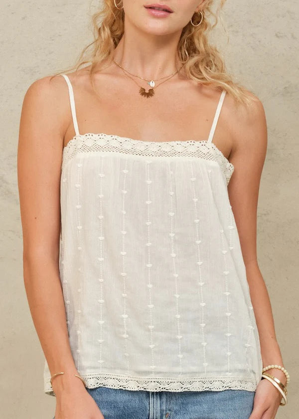 Woman wearing a white lace-trimmed top against a neutral background