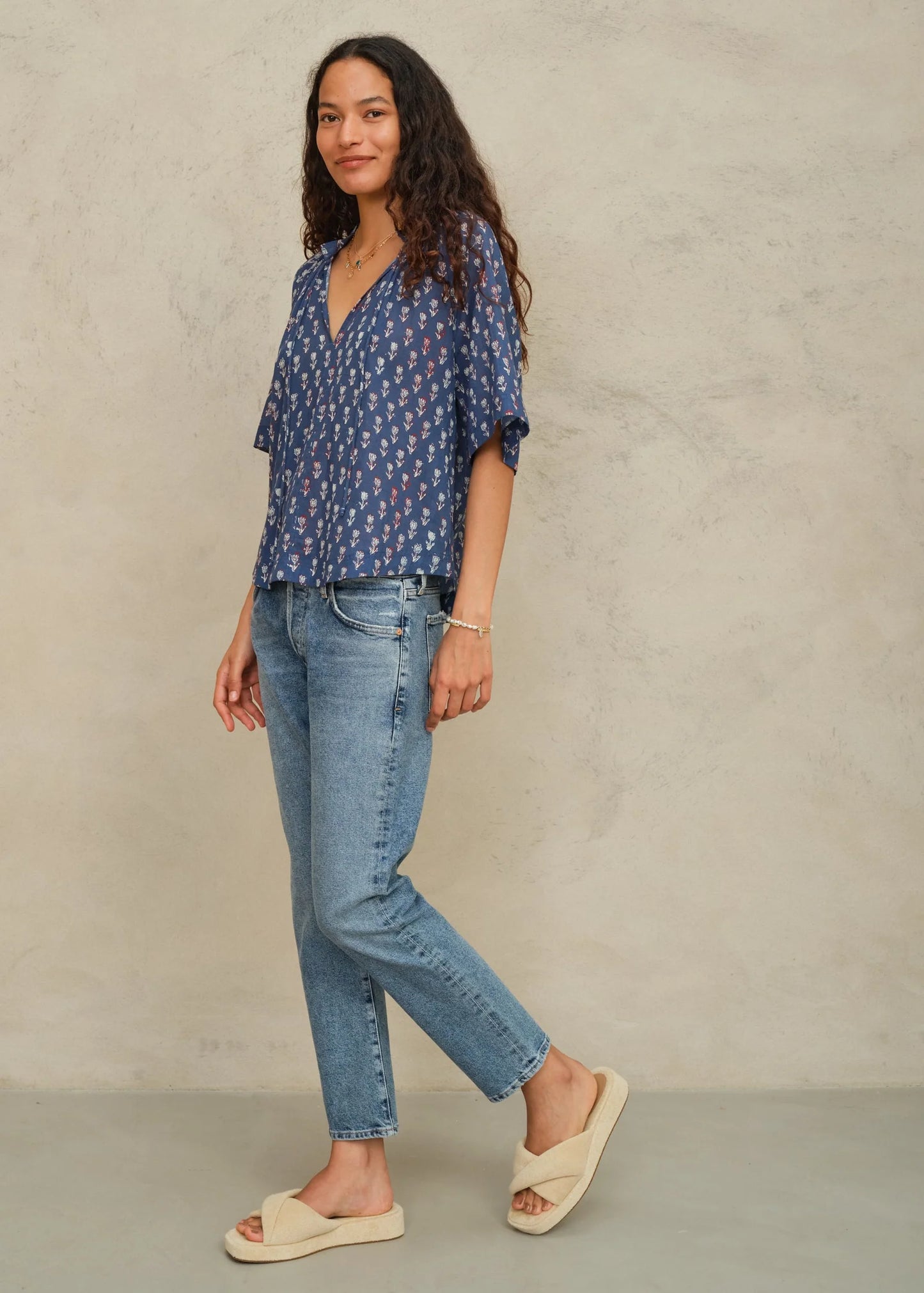 Woman wearing a blue patterned blouse and jeans against a beige background