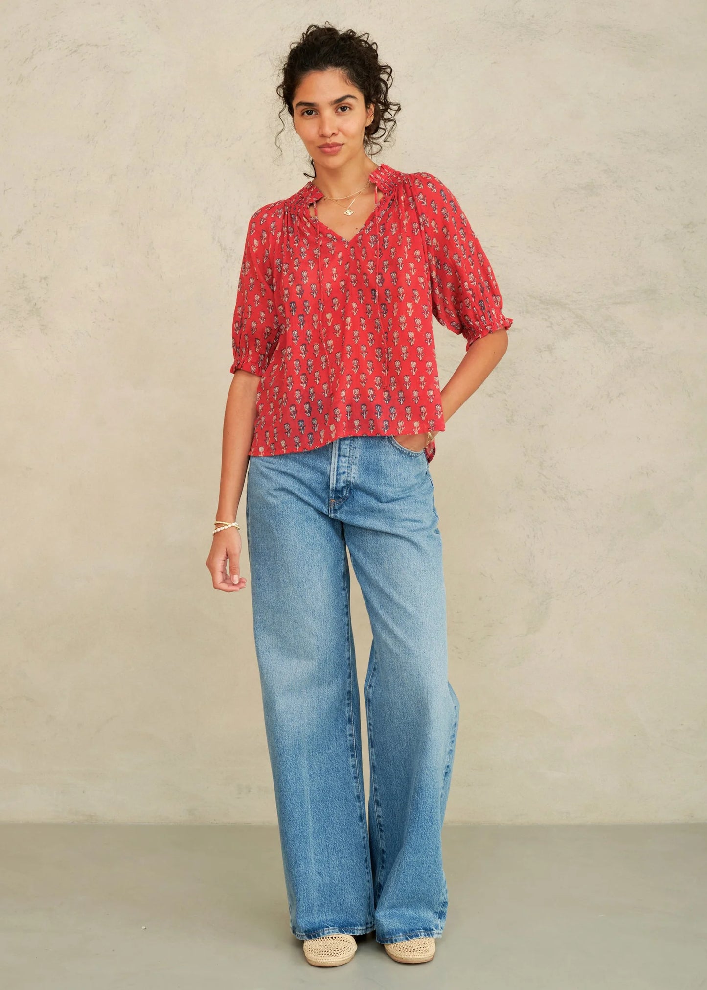 Woman wearing a red patterned blouse and blue jeans against a neutral background