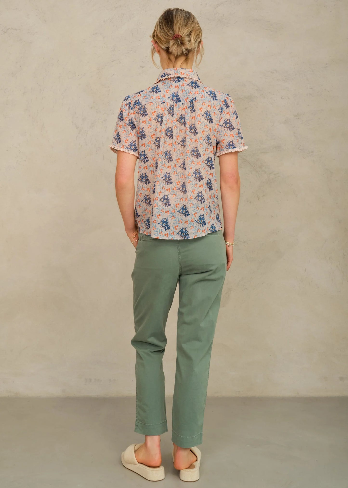 Person wearing a floral shirt and green pants against a beige background