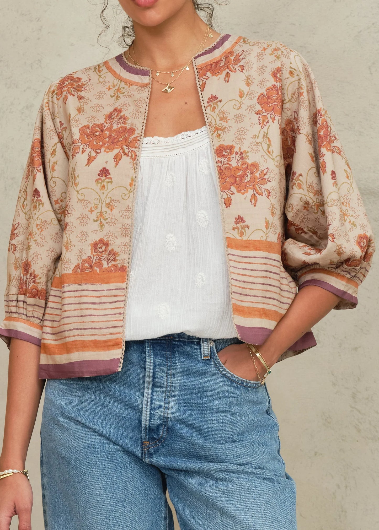 Person wearing a floral patterned cardigan over a white top and blue jeans on a neutral background