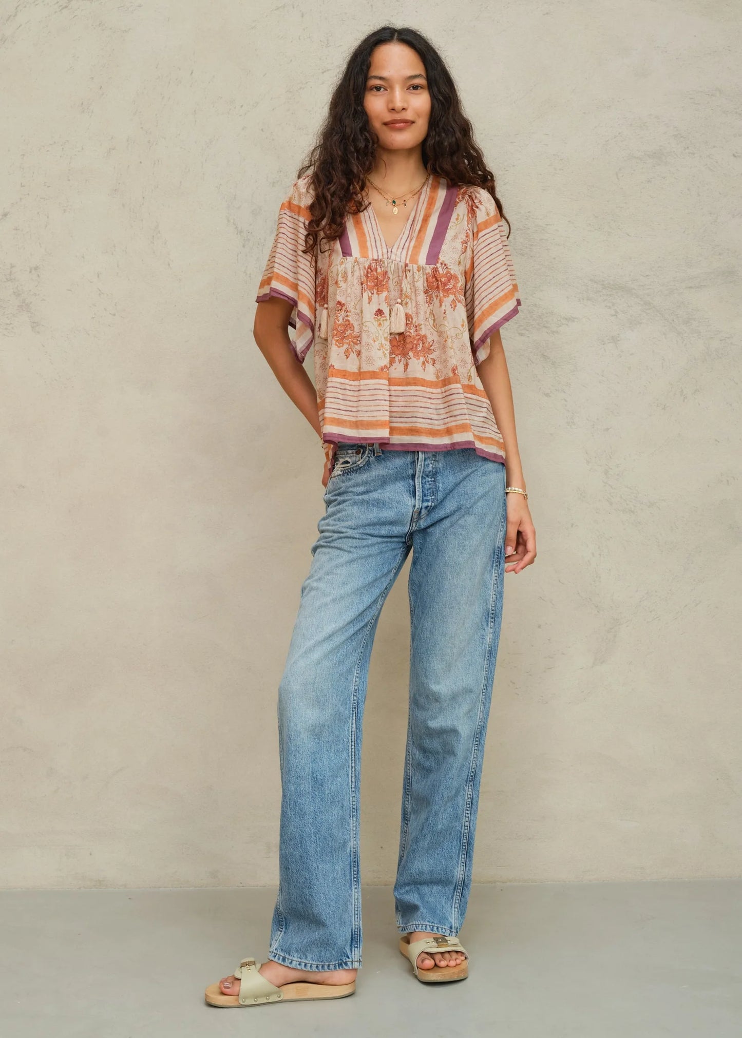 Woman wearing a patterned top and blue jeans against a neutral background