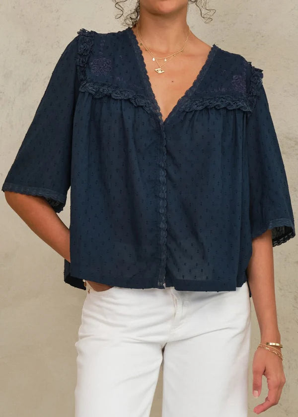 Navy blue blouse with ruffled details worn by a person on a neutral background