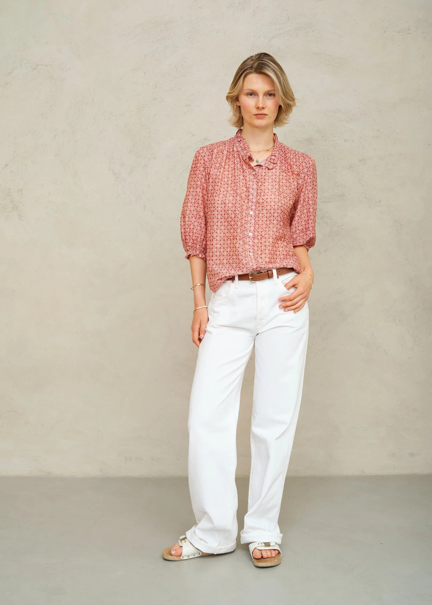 Woman wearing a red patterned shirt and white pants against a beige background