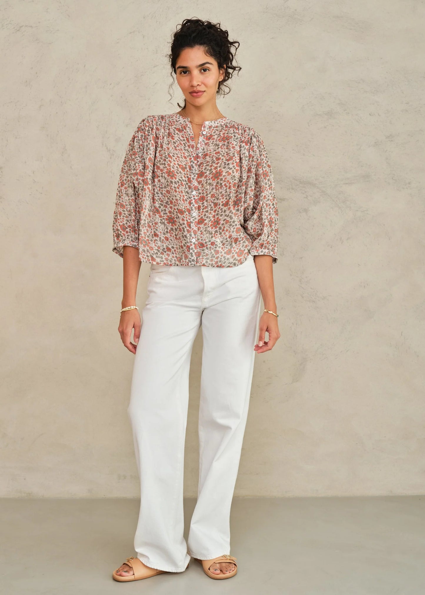 Woman wearing a floral blouse and white pants against a neutral background
