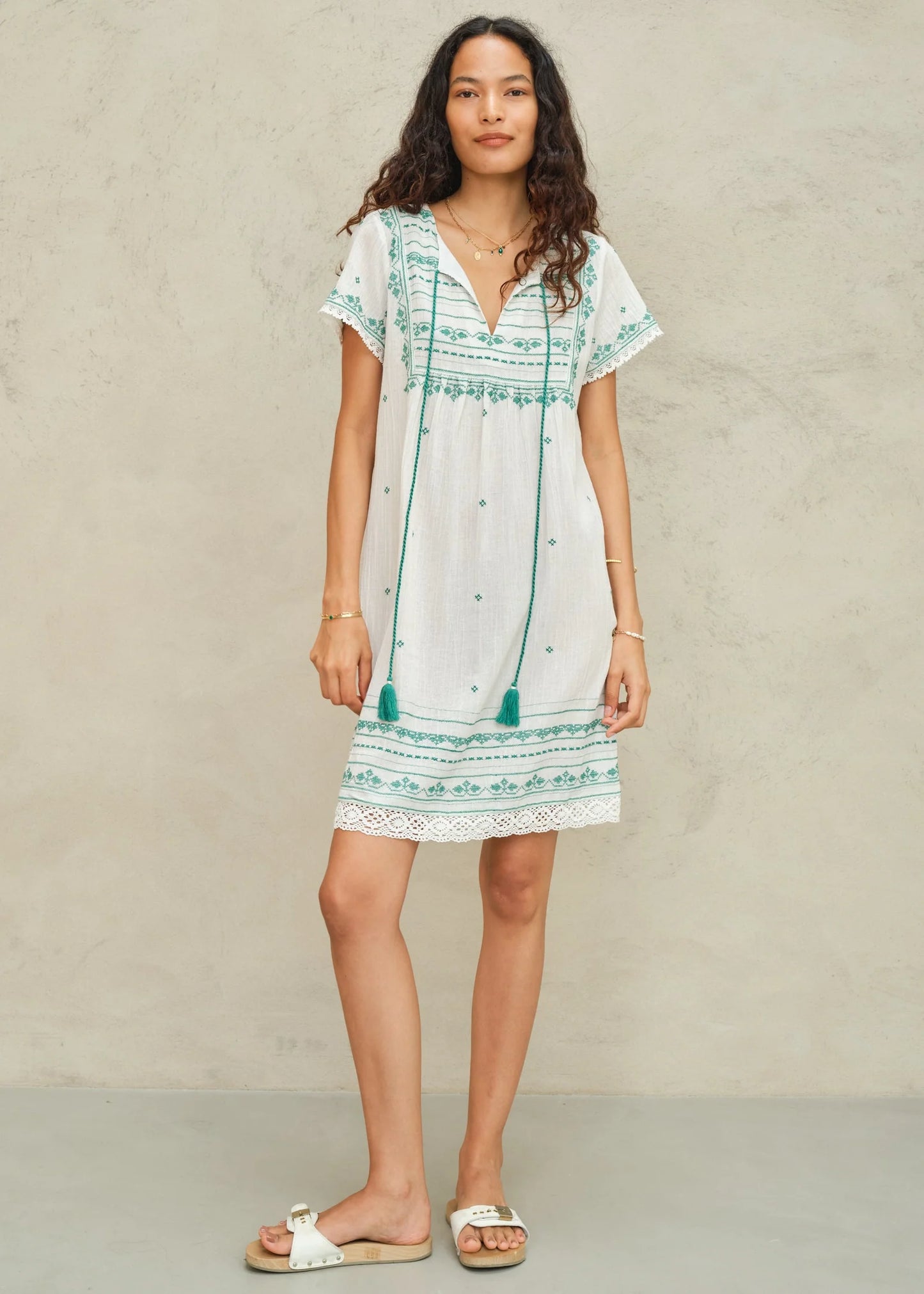 Woman wearing a white dress with green patterns against a beige background