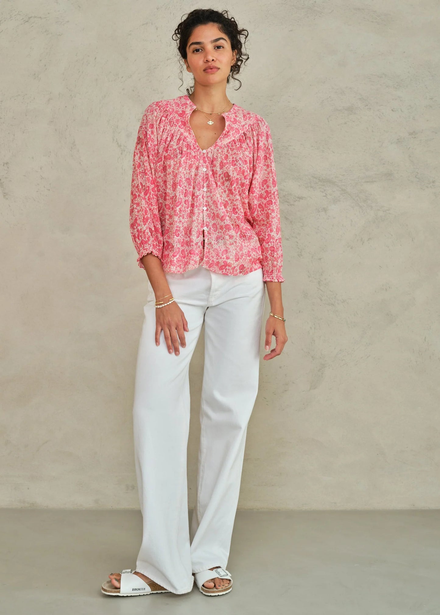 Woman wearing a pink floral blouse and white pants against a beige background