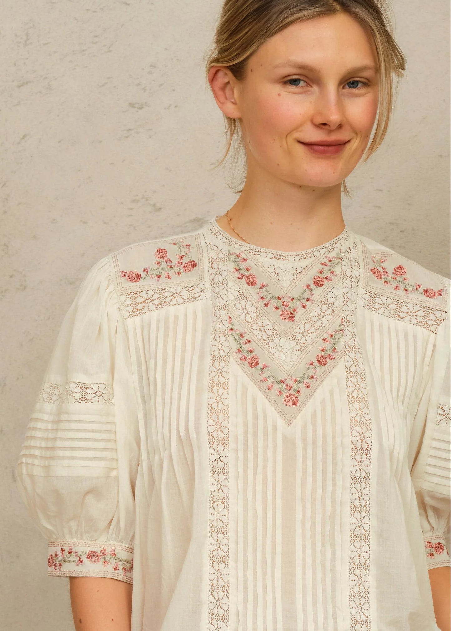 Woman wearing a white blouse with floral embroidery against a plain background