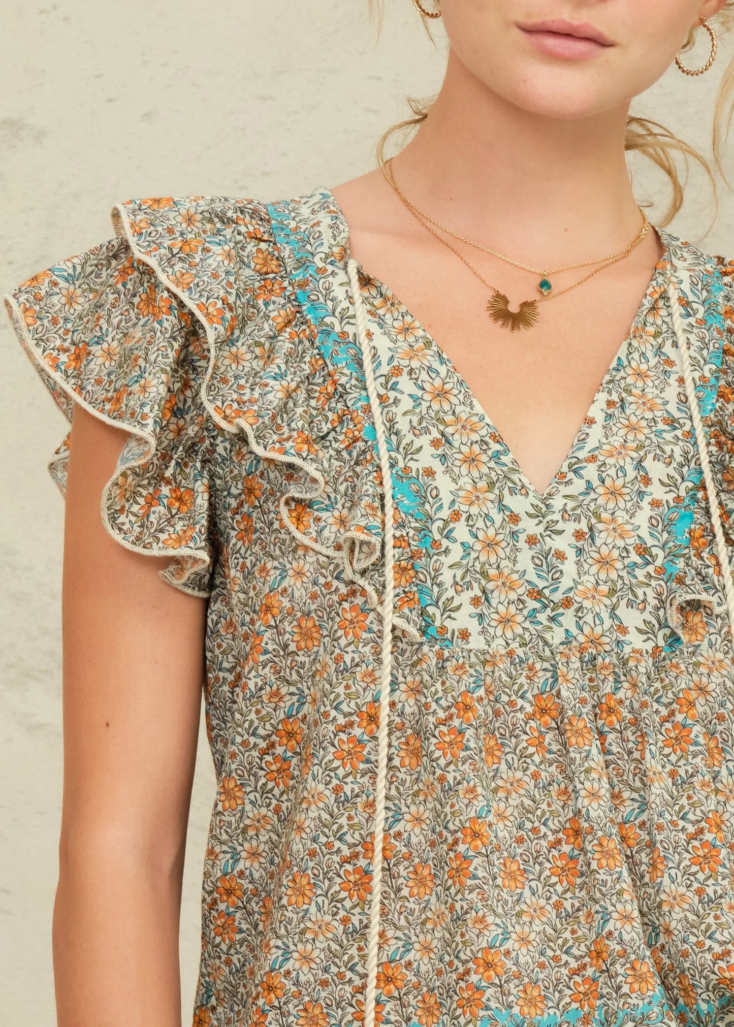 Woman wearing a floral dress with ruffled sleeves against a neutral background