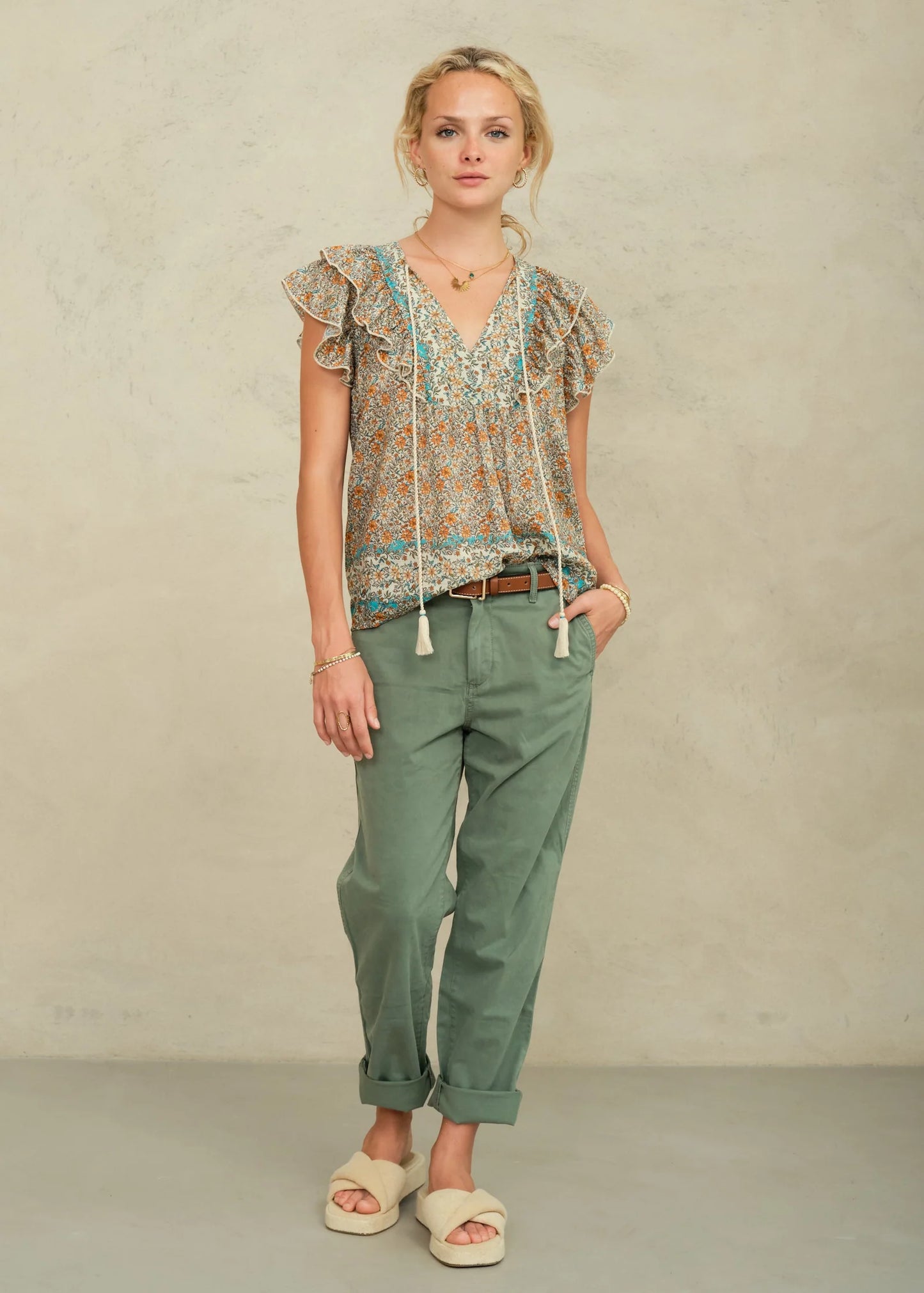 Woman wearing a patterned blouse and green pants against a plain background