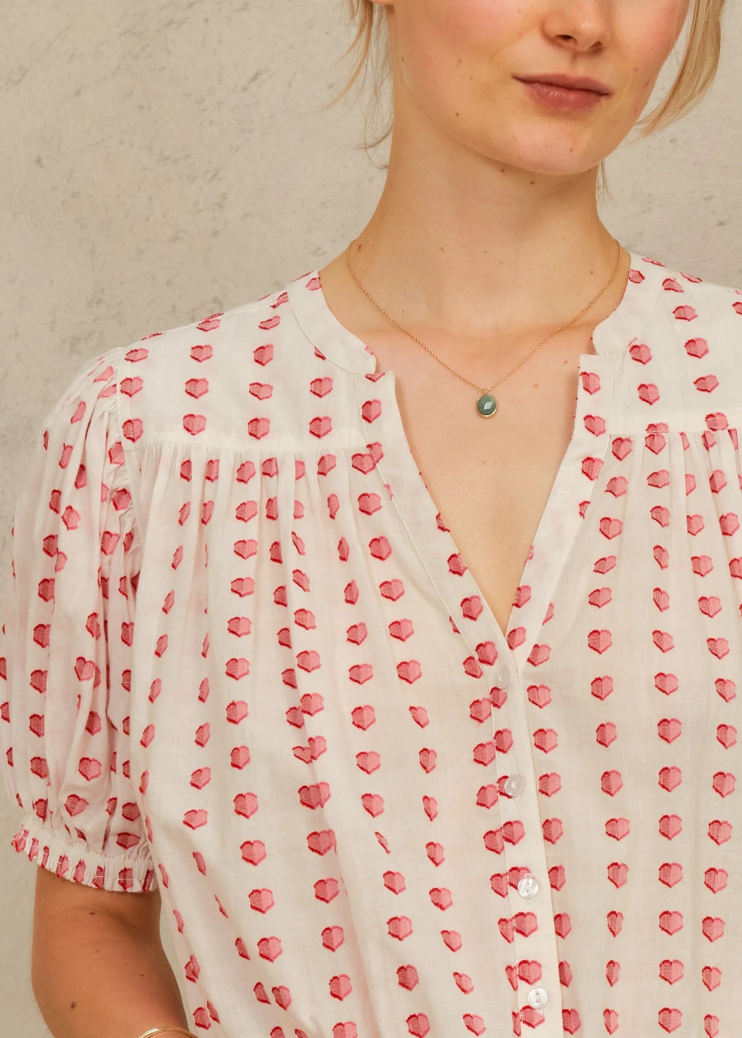 Woman wearing a white blouse with red heart pattern against a neutral background
