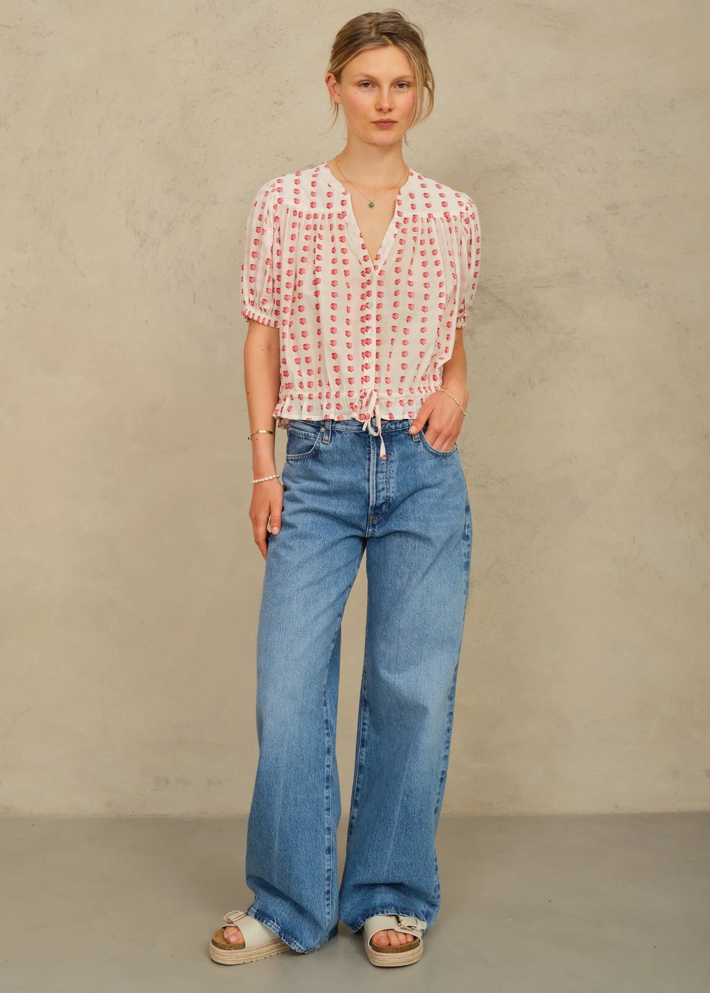 Woman wearing a red and white patterned blouse and blue jeans against a beige background