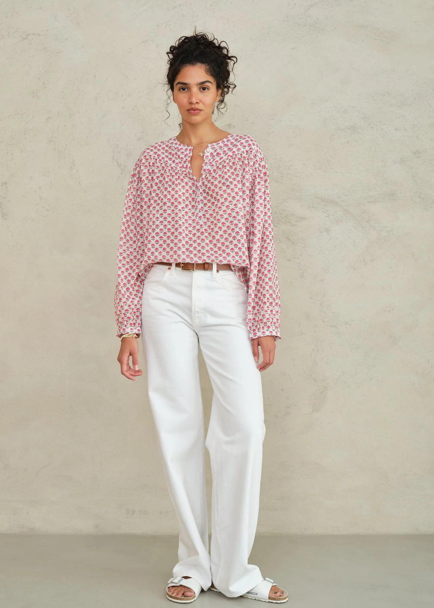 Woman wearing a red patterned blouse and white pants against a beige background