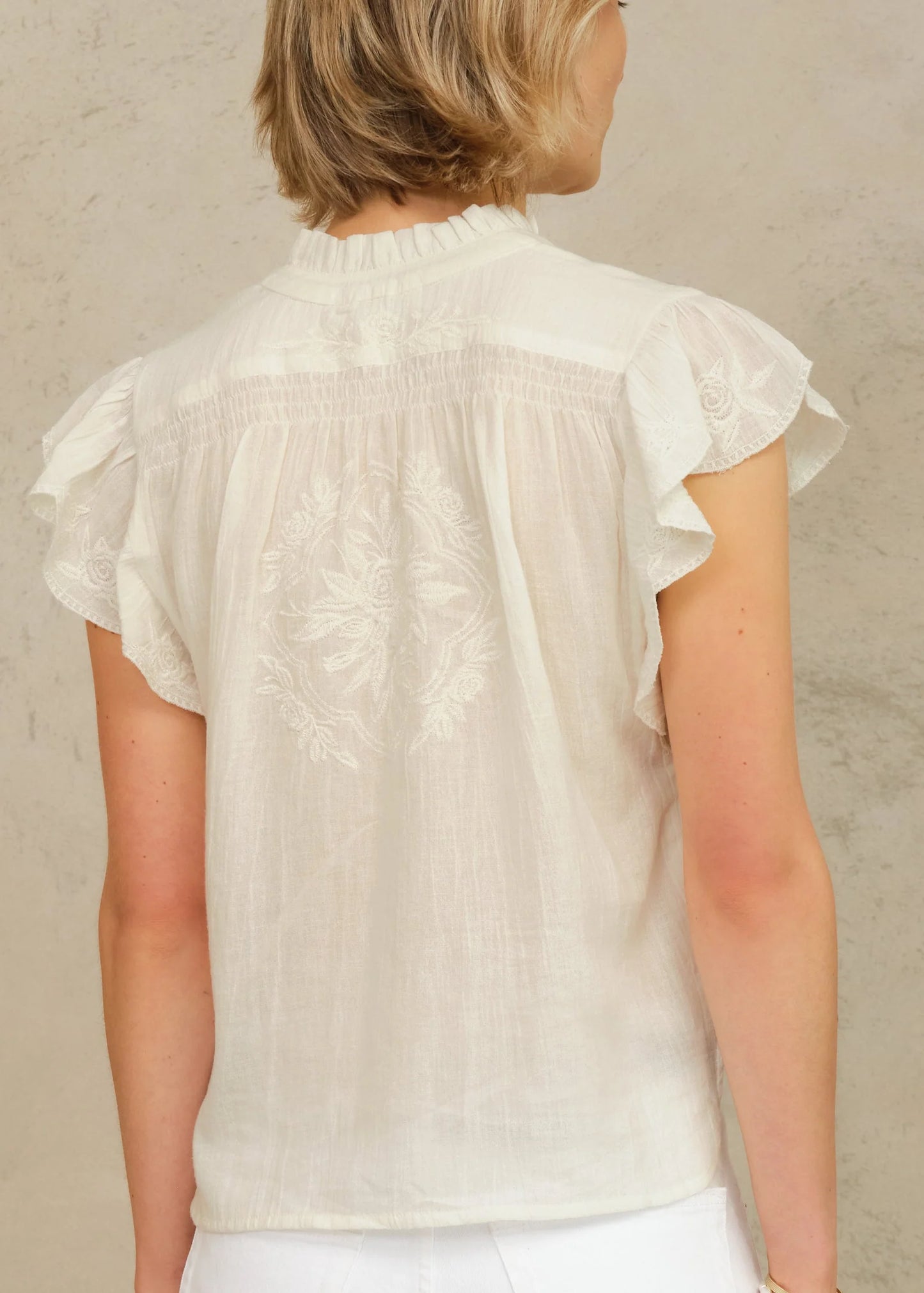 Woman wearing a light-colored blouse with ruffled sleeves against a neutral background