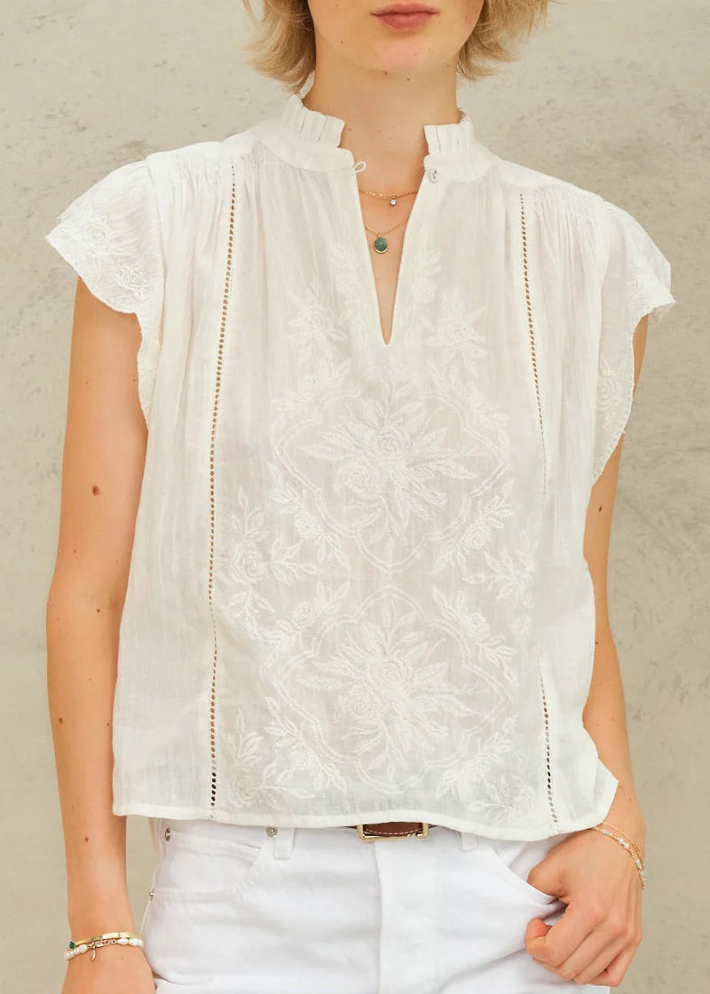 Woman wearing a white lace top and white pants against a neutral background