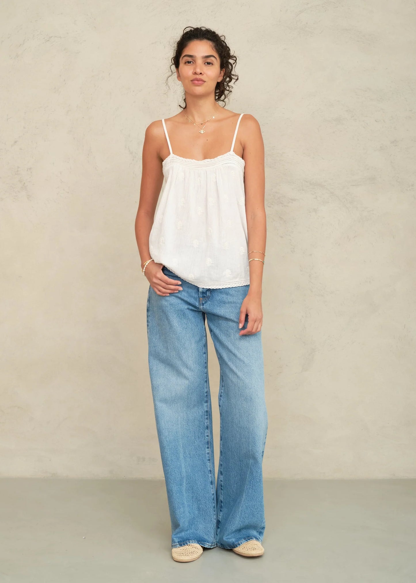 Woman wearing a white top and blue jeans against a plain background