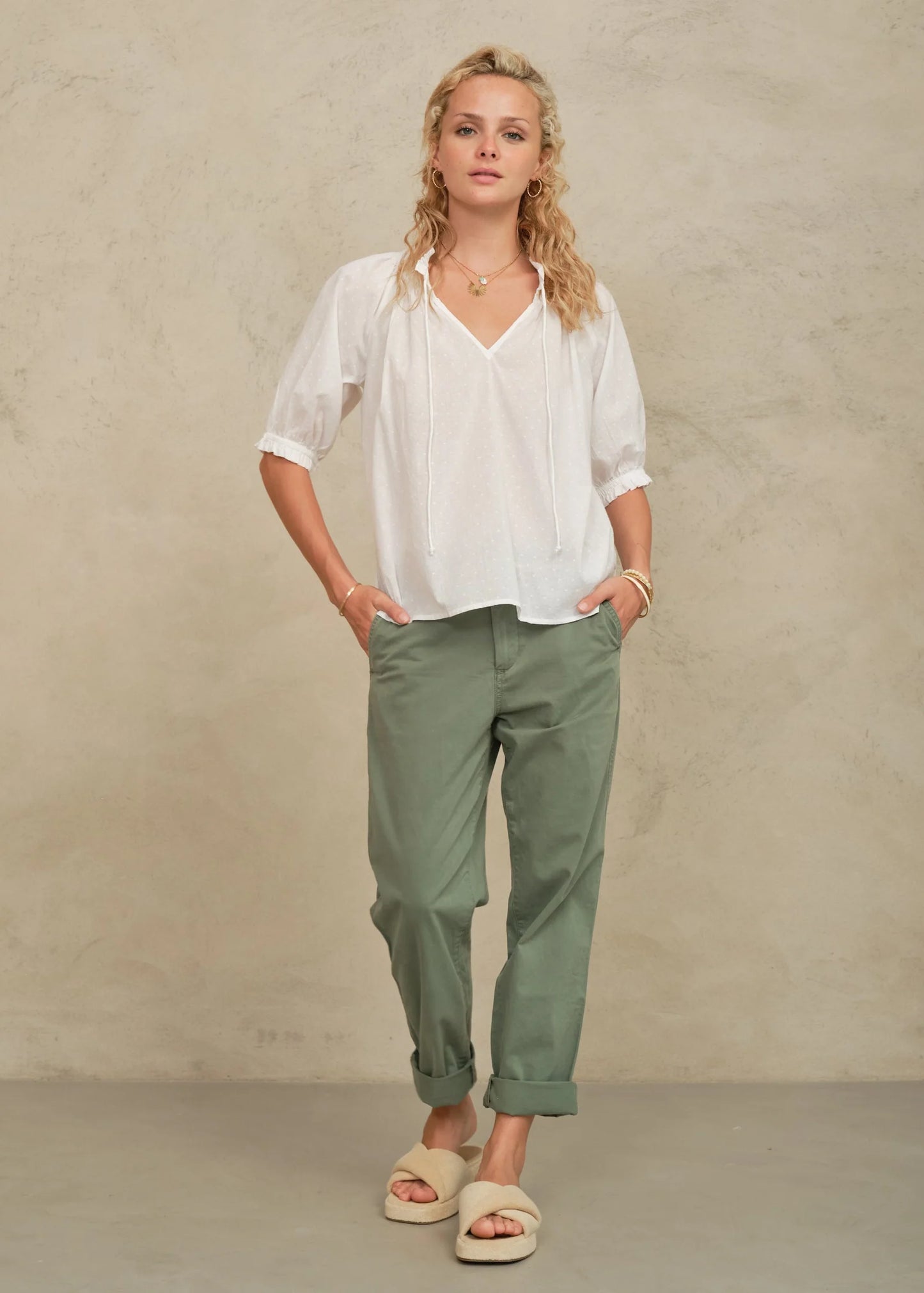 Woman wearing a white blouse and green pants against a beige background