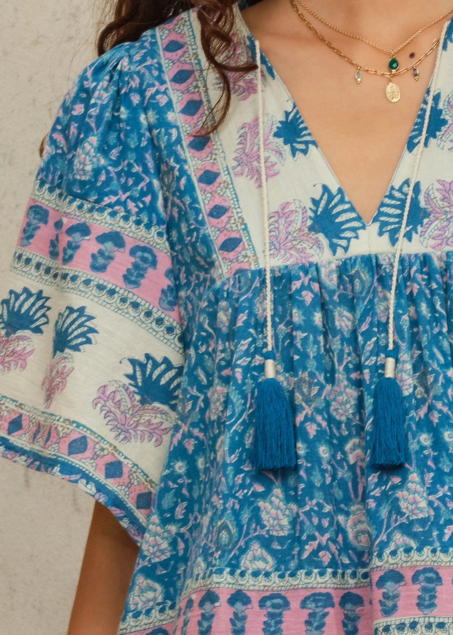 Woman wearing a blue and pink patterned dress with tassel details.