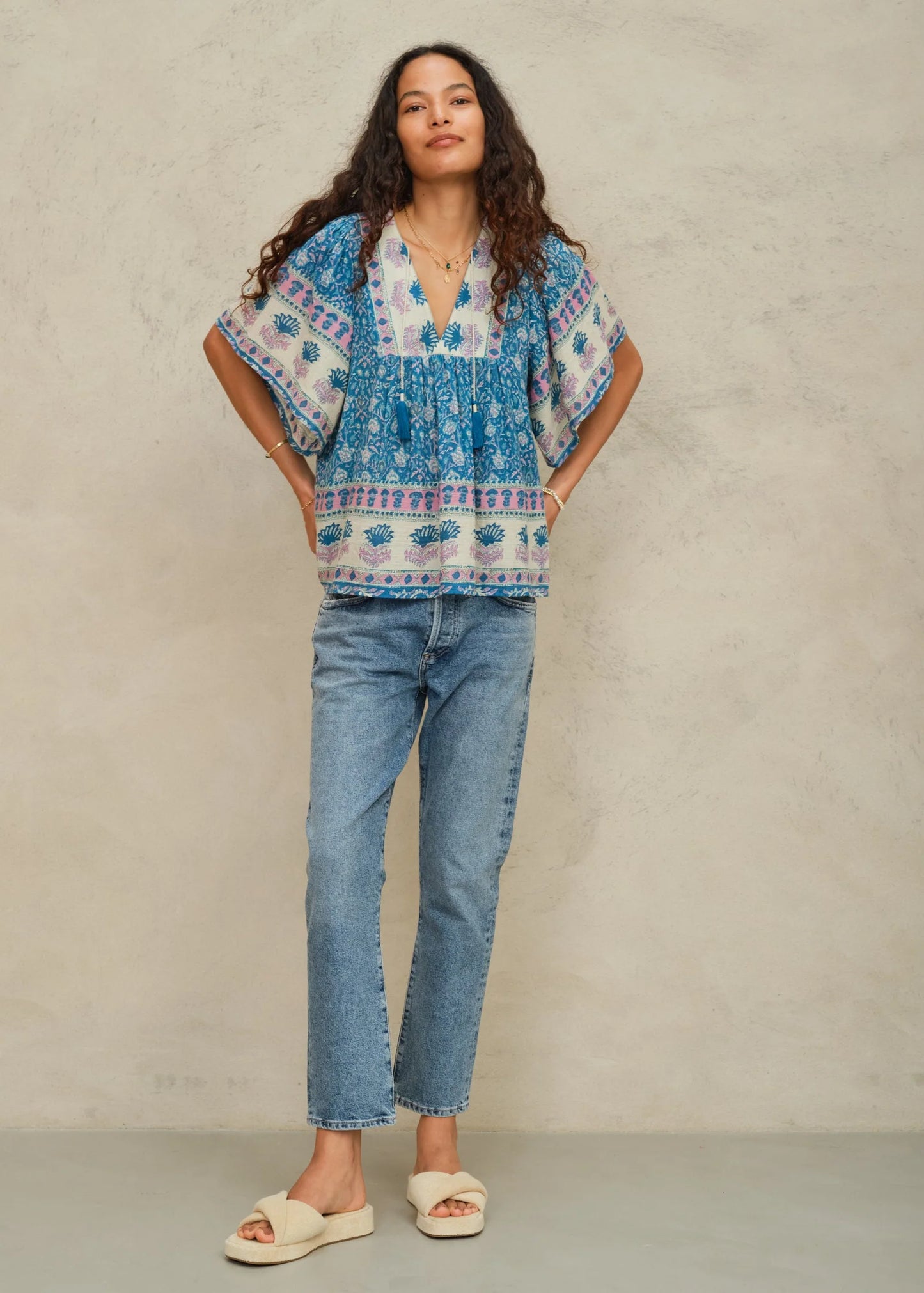 Woman wearing a blue patterned blouse and jeans against a neutral background