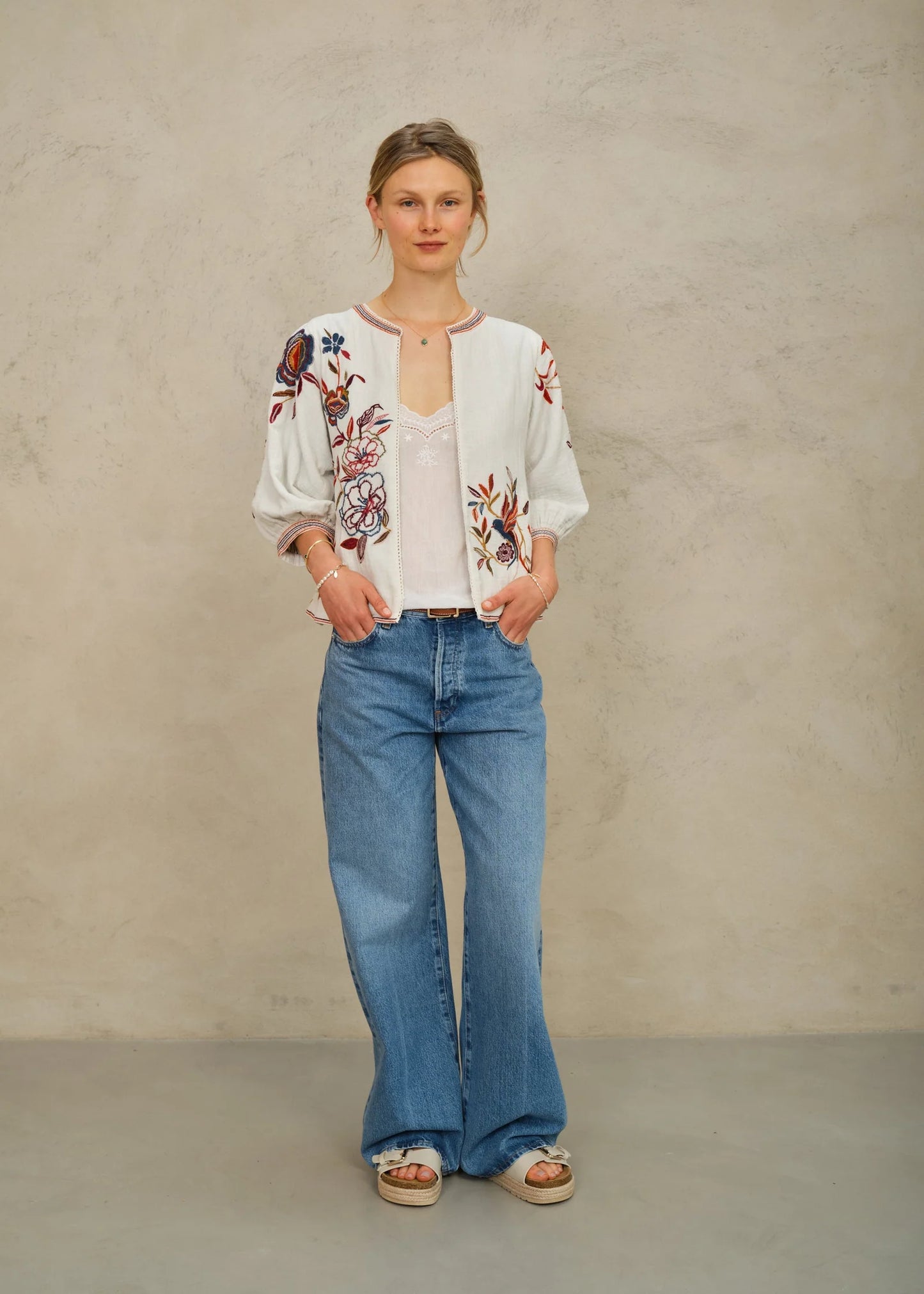 Woman wearing a floral embroidered top and blue jeans against a plain background