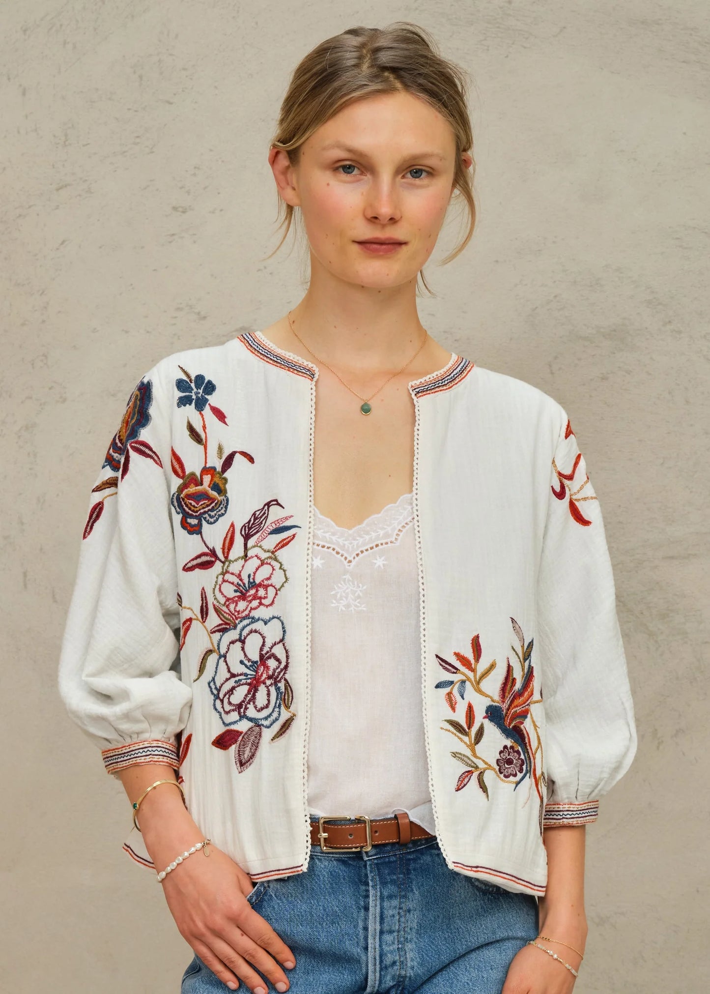 Woman wearing a white embroidered blouse with floral patterns on a plain background