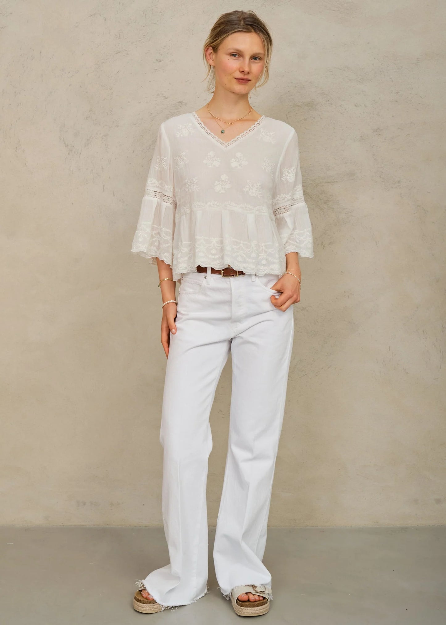 Woman wearing a white blouse and pants against a beige background
