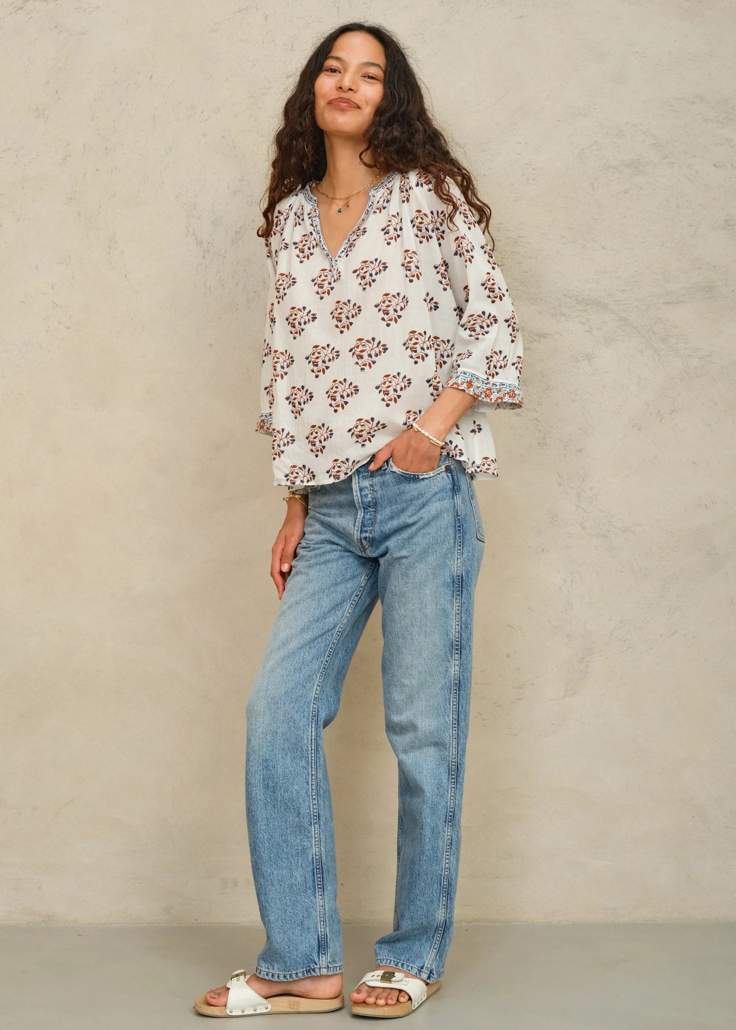 Woman wearing a patterned blouse and jeans against a neutral background
