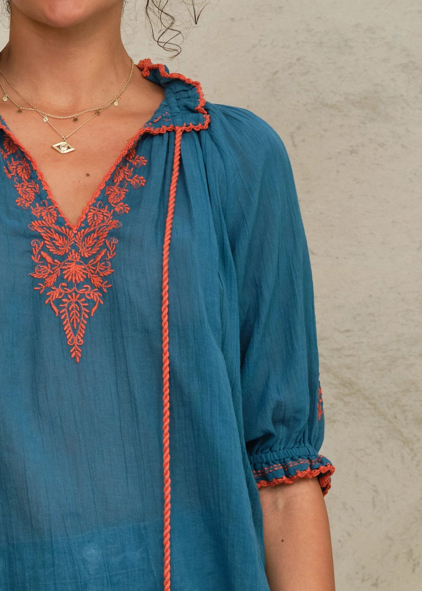 Blue dress with orange embroidery and trim on a neutral background