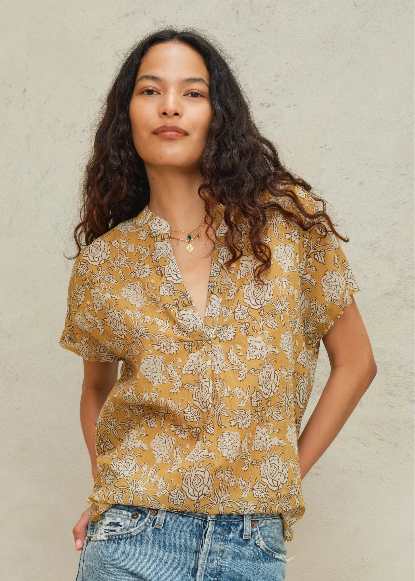 Woman wearing a yellow floral blouse and blue jeans against a beige background