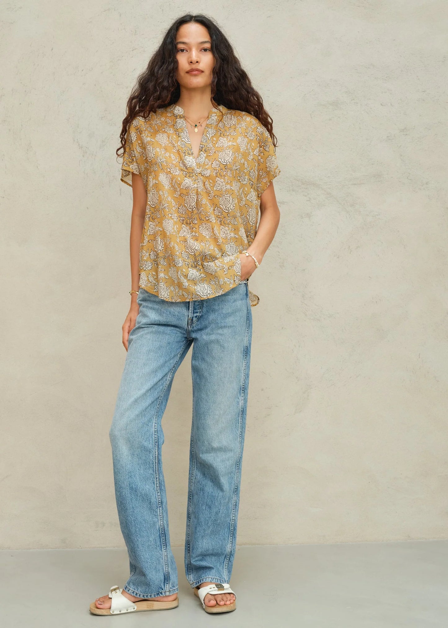 Woman wearing a yellow floral blouse and blue jeans against a beige background
